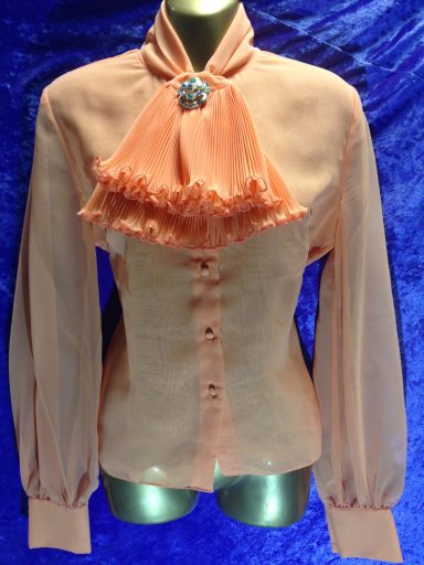 Peach-coloured blouse with high neck, frill detail, and button closure.
