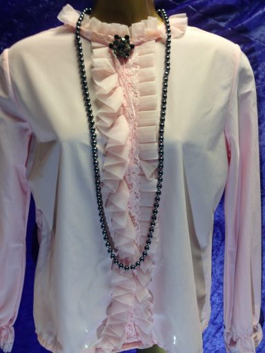 Light pink blouse with ruffled front and a decorative necklace.
